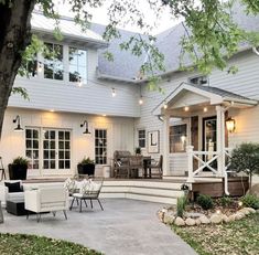 a large white house with lots of windows and furniture on the front porch, surrounded by trees