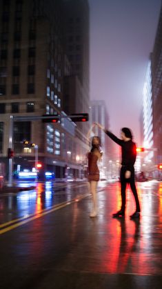 two people are dancing in the rain on a city street at night with traffic lights