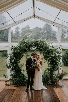 a bride and groom standing in front of an arch with greenery at their wedding