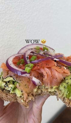 someone is holding up a sandwich with salmon and onions on it