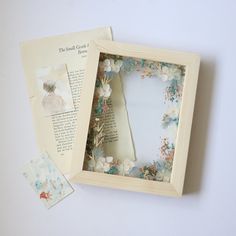 an open book with flowers on it and some pictures in the box next to it