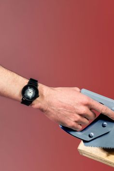 a person holding a knife on top of a piece of wood next to a watch