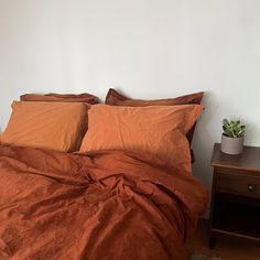 a bed with orange sheets and pillows on top of it next to a night stand