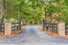 a gated driveway leading into a wooded area with stone pillars and gates on either side