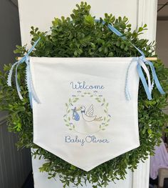 a welcome baby banner hanging on a door with blue ribbon and green leaves around it