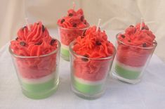 four glasses filled with red and green desserts on top of a white table cloth