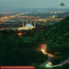 the city lights shine brightly in the distance as cars drive down a winding road at night