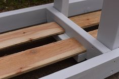 a wooden bench sitting on top of a cement ground next to a white fence and grass