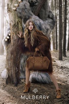 a woman standing in front of a tree with a large stuffed animal behind her and holding a brown purse