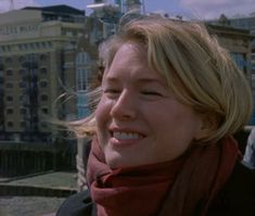 a woman with blonde hair smiling and wearing a red scarf on her neck, in front of a cityscape