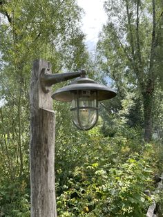 an old fashioned light hanging from the side of a wooden post in front of trees