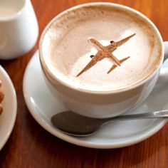 a cup of coffee with an airplane drawn in it on a saucer next to a plate of doughnuts