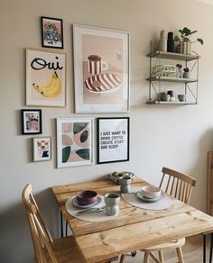 a wooden table with plates and cups on it in front of pictures hanging on the wall