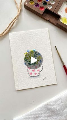 a card with a potted plant on it next to paintbrushes and watercolors