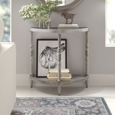 a white console table with flowers and books on it in front of a mirror, framed art