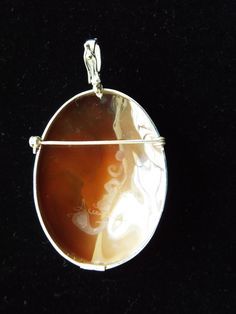 a pendant is shown on a black surface with an orange stone in the shape of a woman's face