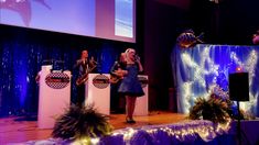 two women are singing on stage at an event with balloons and streamers in the background