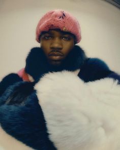 a man in a pink hat and blue coat holding a large white fur ball on his chest