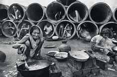 black and white photograph of people sitting in front of large pipes