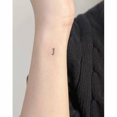 a small anchor tattoo on the left inner arm, with a tiny letter in the middle