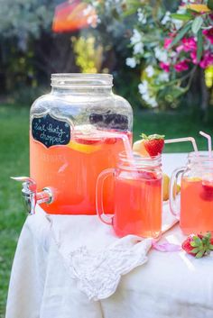 two mason jars with strawberries and lemonade sit on a table in the garden