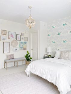 a white bed sitting under a chandelier next to a wall with pictures on it