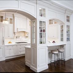 a kitchen with white cabinets and wood flooring is pictured in this image, there are two stools at the center of the island