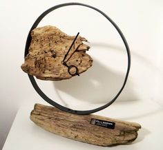 a piece of wood with a metal clock on it's face sitting next to a piece of driftwood