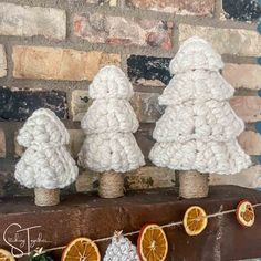 three crocheted christmas trees sitting on top of a wooden table next to an orange slice