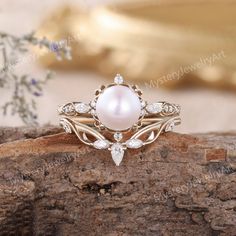 a pearl and diamond ring sitting on top of a piece of wood with flowers in the background