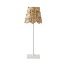 a lamp that is on top of a white base and has a wicker shade