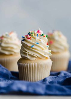 three cupcakes with white frosting and sprinkles on a blue napkin