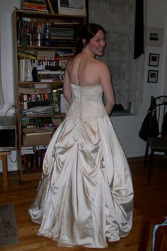 a woman in a wedding dress standing on a wooden floor next to a bookshelf