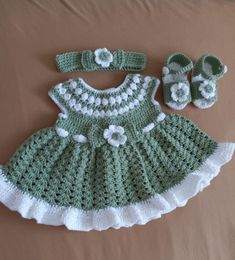 a green and white crocheted dress, booties and hat on a bed