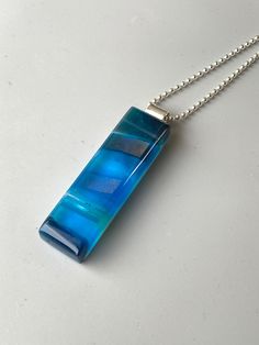 "Colorful waves of aqua, sea blue and turquoise glass combine with shimmery bands of dichroic and iridescent glass to create the impressionistic pendant on this necklace. The depth and variety of colors in the glass create a striking, one-of-a-kind kiln-fired pendant. Glass is kiln fired, shaped with beveled edges, and then fire polished in my glass studio. Pendant hangs from a sterling silver bail on a sterling silver bead chain. Pendant is also available in green, olive green, cobalt blue, bla Modern Blue Pendant Jewelry, Modern Blue Round Pendant Necklace, Modern Turquoise Glass Jewelry, Unique Blue Rectangular Pendant Jewelry, Modern Blue Rectangular Necklace, Blue Rectangular Pendant Necklace, Unique Blue Rectangular Pendant Necklace, Blue Recycled Glass Pendant Necklace, Modern Blue Necklaces As A Gift