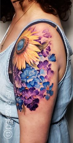 a woman with a sunflower and blue flowers on her left upper half sleeve tattoo