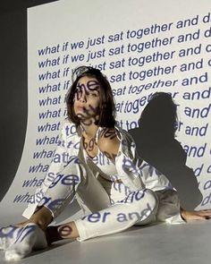 a woman sitting on the ground in front of a wall with words painted on it