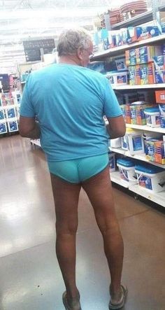 an older woman in blue shorts is looking at toilet paper on the shelf inside a store