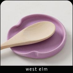 two wooden spoons sitting on top of a purple plate with the words west elm written below it