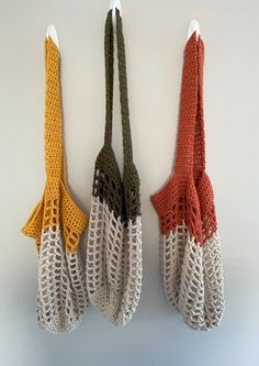 three crocheted gloves hanging from hooks on a white wall next to each other