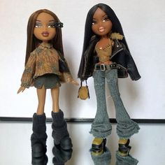 two dolls standing next to each other in front of a white wall and one is holding a purse