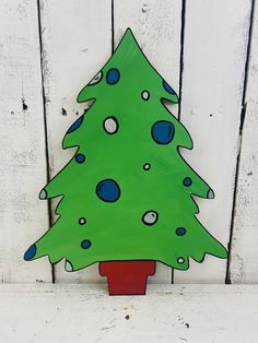 a green painted christmas tree sitting on top of a red pot next to a white fence