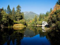 a body of water surrounded by trees and mountains in the distance with a large rock sticking out of it's surface