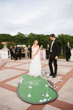 a bride and groom are playing golf on the green in front of their wedding party