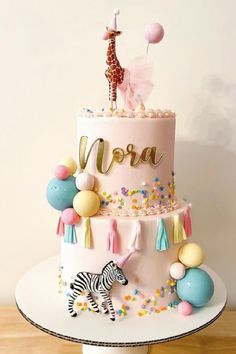 a three tiered cake with a giraffe and balloon decoration on the top