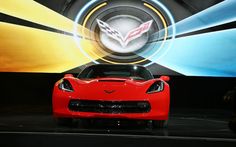 a red sports car is on display in front of a large screen with the corvette logo