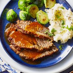 a blue plate topped with meat, mashed potatoes and brussel sprouts