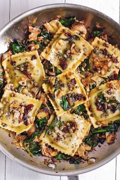 a pan filled with ravioli and spinach covered in cheese, meat and seasoning