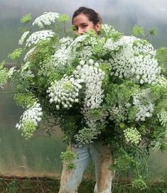 a woman holding a bunch of white flowers in front of her face and behind her head