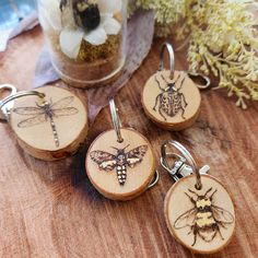 three wooden key chains with bees on them sitting on a table next to some flowers